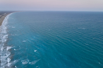 Fototapeta na wymiar White foamy sea waves splash to sandy beach in the evening. Evening surf. Aerial top view from UAV drone