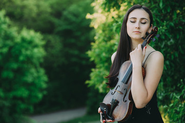 Fototapeta na wymiar Beautiful girl with dark hair holds an old violin in her hands. Violinist