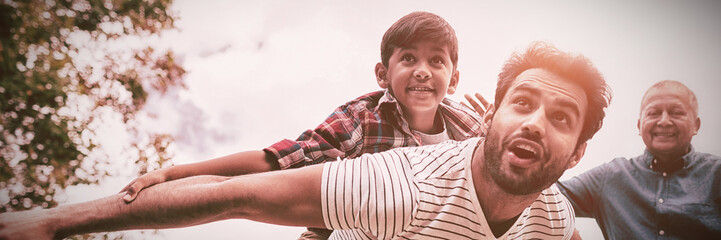 Smiling grandfather looking at man giving piggy backing to son