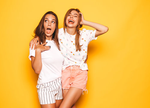 Two young beautiful smiling hipster girls in trendy summer clothes. Sexy carefree women posing near yellow wall in studio. Positive models going crazy and having fun.Hugging