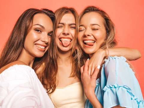 Three young beautiful smiling hipster girls in trendy summer clothes. Sexy carefree women posing near pink wall in studio. Positive models going crazy.Taking selfie self portrait photos on smartphone