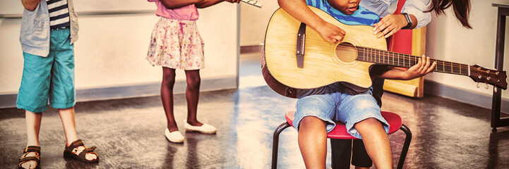 Teacher assisting a kids to play a musical instrument in classroom