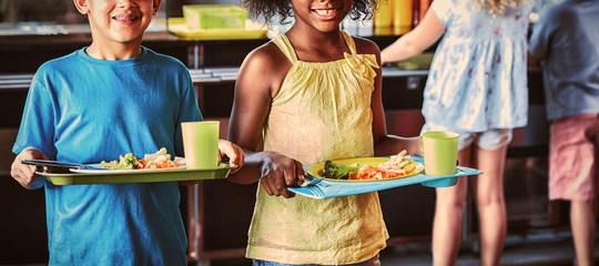 Happy school children holding food tray in canteen © vectorfusionart