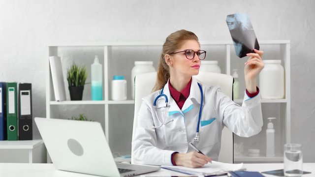 Busy female surgeon checking x-ray image taking note working at modern clinic room