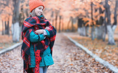 Girl in autumn city park in leaf fall. Young beautiful mother with her daughter on nature. A girl in a hat walks in the park.