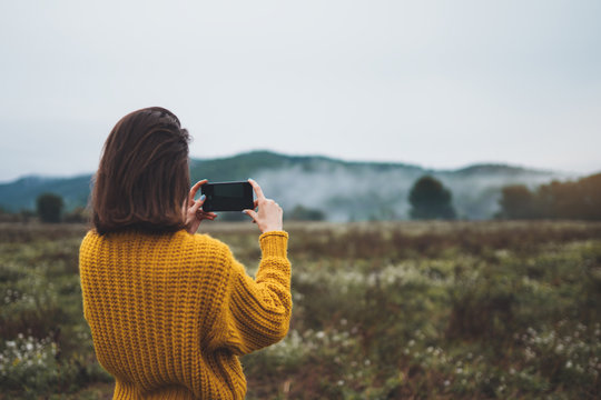 photographer girl hold in hands mobile phone taking photo on smartphone autumn froggy mountain, tourist shooting on photo camera on background landscape, internet online concept