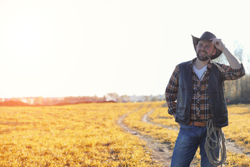 Naklejka na ściany i meble A man cowboy hat and a loso in the field. American farmer in a field wearing a jeans hat and with a loso. A man is walking across the field in a hat