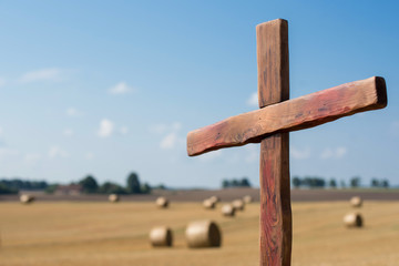 Wooden Christian cross on a field full of bales of hay on a sunny day
