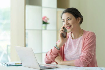 Caucasian successful businesswoman talking on phone and working on laptop computer at home office.