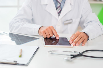 Senior doctor at his office in hospital working close-up using digital tablet