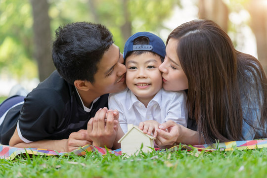 Happy young asian family, father and mather kiss son together, having fun outside together picnic in the park.