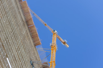 The construction of a multistory building against the blue sky, stands next to a yellow tower crane. Photo bottom up