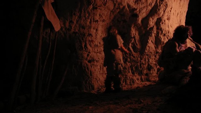 Primitive Prehistoric Neanderthal Child Wearing Animal Skin Draws Animals and Abstracts on the Walls at Night. Creating First Cave Art with Petroglyphs, Rock Paintings. Back View Following Shot