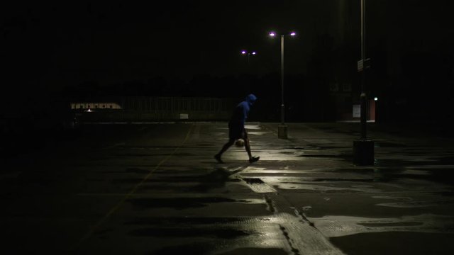 Basketball player dribbling the ball in an empty car park at night under a street light