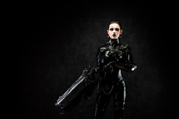 Obraz premium Portrait of a young woman in latex jumpsuit holding a big futuristic weapon in her hands