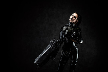 Portrait of a young woman in latex jumpsuit holding a big futuristic weapon in her hands