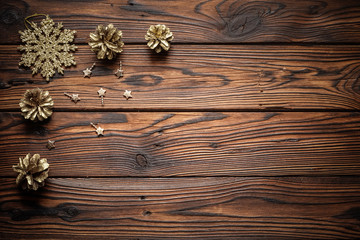 Gilded pine cones, metal stars and sparkling snowflake Christmas ornament on the dark brown plank wooden surface.