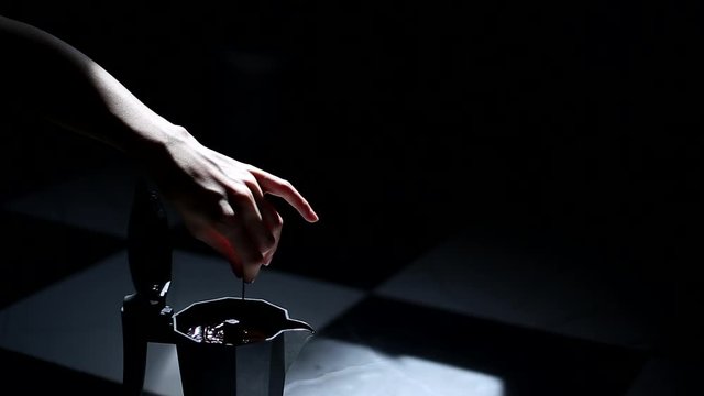 Close-up of female hand who stir coffee in moka pot, on dark background.