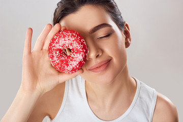 Young Woman  Covered Her Face with Pink Donut in Home Kitchen. Brunette Girl Tastes a Donut. Sweets Are Unhealthy Junk Food. Dieting, Healthy Eating, Lifestyle. Weight Loss.