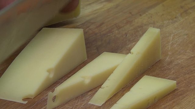 Closeup of man with knife on wooden desk, cuts cheese in small pieces.