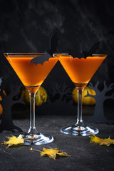 Orange martini cocktails with bats and decor for Halloween party, on dark background