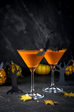 Orange martini cocktails with bats and decor for Halloween party, on dark background