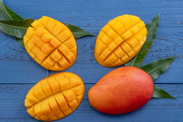 Fresh mango, beautiful chopped fruit with green leaves on dark wooden table background. Tropical fruit design concept. Flat lay. Top view. Copy space