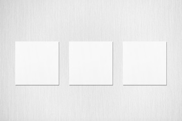 Three empty white square flyer or business card mockups with soft shadows on neutral light grey textured background. Flat lay, top view