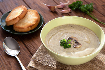 Mushroom cream soup with croutons and garlic on a wooden table.