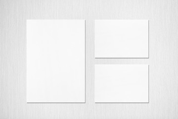 One empty white vertical a4 sized poster and two a5 sized horizontal rectangle card mockups with soft shadows on neutral light grey textured background. Flat lay, top view