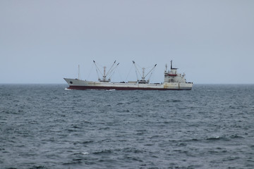 Reefer vessel underway in the ocean. White ship sailing on foggy horizon background.