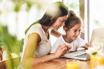 Image of gorgeous family woman and her little daughter smiling and using laptop computer together...