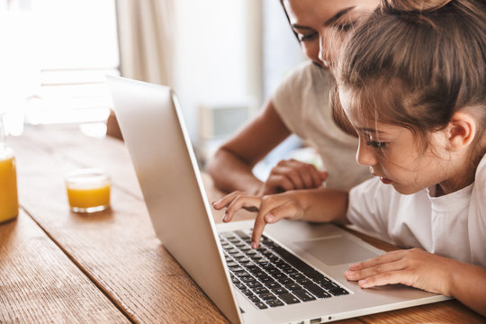 Image of caucasian family woman and her little daughter smiling and using laptop computer together in apartment