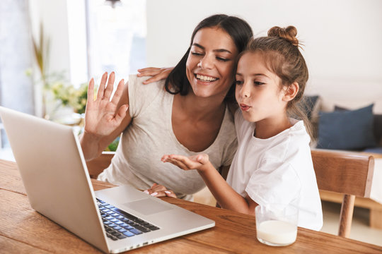 Image of happy family woman and her little daughter smiling and waving at laptop computer together in apartment