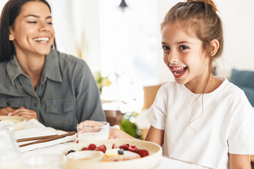 Image of amazing family mother and little daughter having breakfast at home in morning