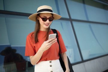 Young woman teenager outdoors looks at the phone. Sunglasses and hat. City Style