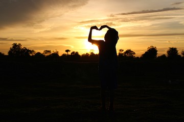 The silhouette of the boy raised his heart-shaped hands and the blue sky, golden yellow sunlight at sunset, taking a blurred photo