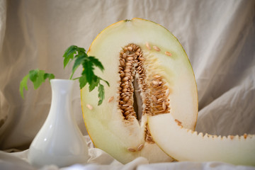 Halved melon, lime and tomato leaves in a vase. Slice of melon in the foreground. Warm tone. On a...