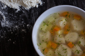 Top view of soup in bowl with dumplings on black background