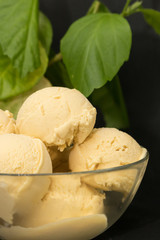 Homemade mango ice cream in yellow in a glass clear deep plate on a black background and green plant