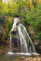 Fototapeta na wymiar Beautiful waterfall at mountain river in colorful autumn forest. Nature landscape