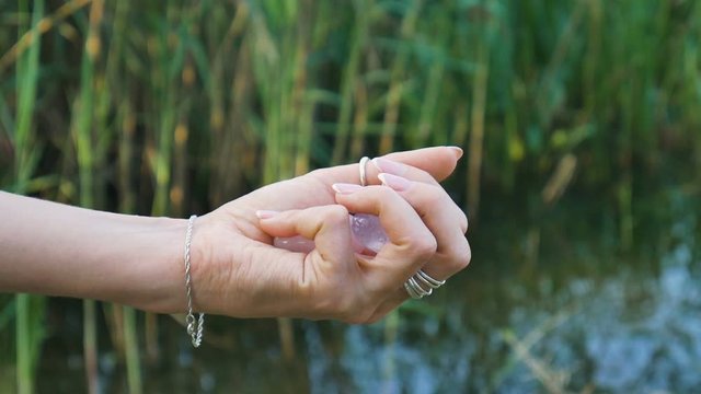 Female hand holding a rose quartz and amethyst crystal yoni eggs on river background. Women's health, unity with nature concepts