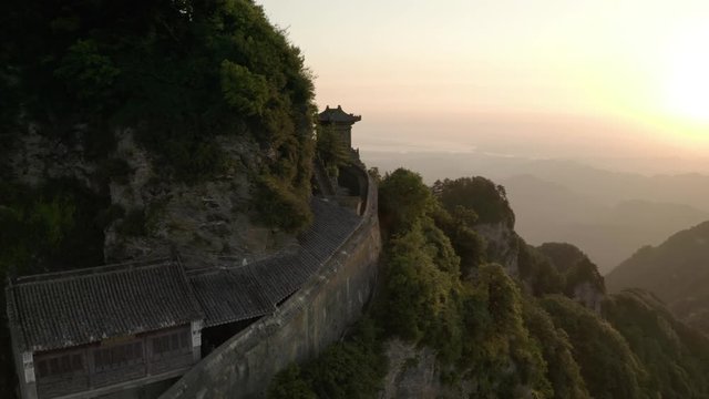 Wudang mountain temple rising aerial view across hazy sunrise horizon overlooking distant mountain ranges.