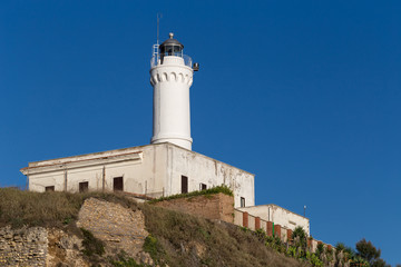 Fototapeta na wymiar Old lighthouse in Anzio city, Lazio region, Italy. Traditional white lighthouse on blue sky background.