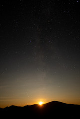 The moon setting behind mountains below a clear stary nights sky