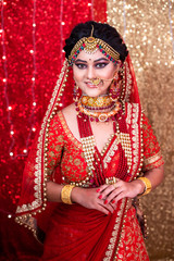 Fototapeta na wymiar Portrait of a beautiful Indian model in Traditional bridal makeup with red lehanga & heavy Gold and Diamond jewelry.