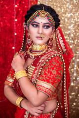Fototapeta na wymiar Portrait of a beautiful Indian model in Traditional bridal makeup with red lehanga & heavy Gold and Diamond jewelry.