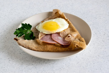 Galette bretonne with ham and fried eggs on a white background.