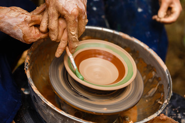 A potters hands guiding a child hands to help him to work with the ceramic wheel