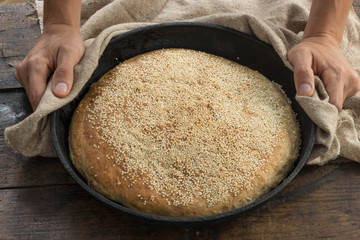 Male hands holding whole grain homemade bread in round baking tray rustic style